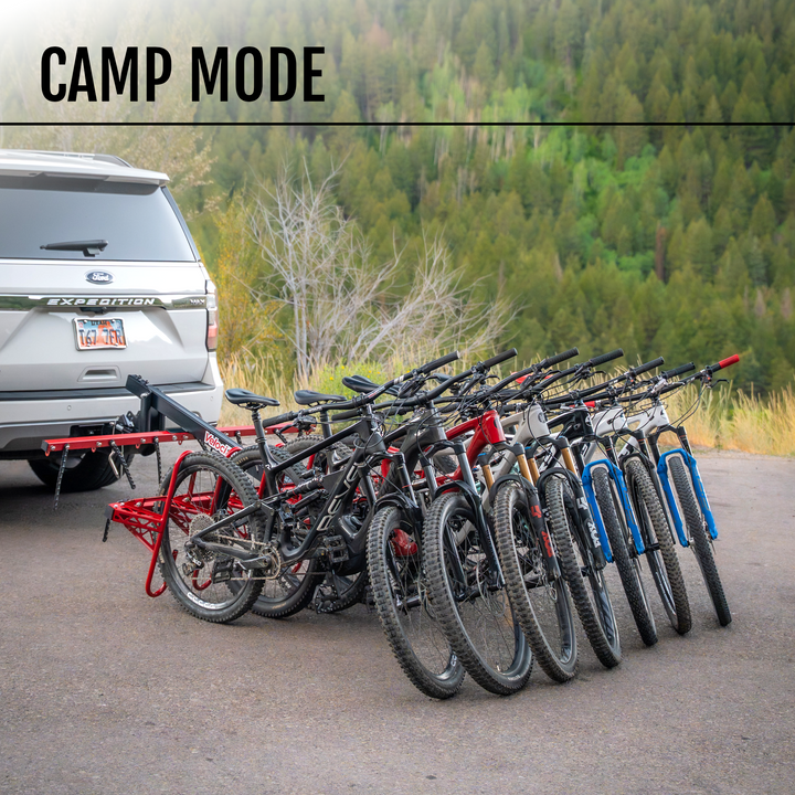 Row of bicycles racked on a MAX rack on a vehicle with a forest in the background, labeled 'Camp Mode'.