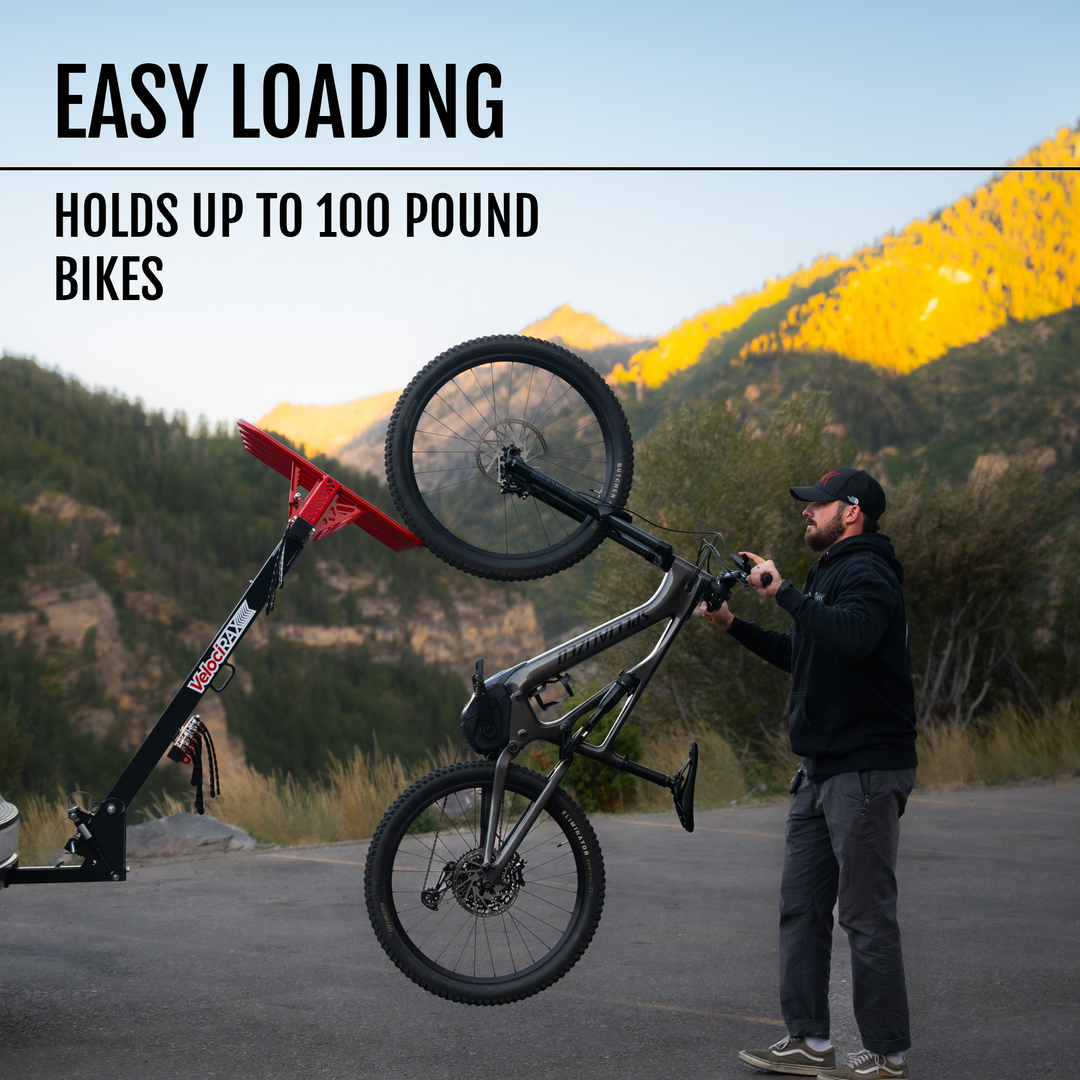 Person loading a bicycle onto a bike carrier with mountains in the background